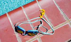 Goggles on pool deck with yellow seahorse goggle tag to identify the owner of the goggles. Goggle tags are made by Swim Loops. www.swimloops.com