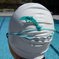 Sea foam green alligator Swim Loops goggle tag with name written on it attached to swim goggles on swimmers head