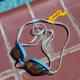 Yellow unicorn shaped Swim Loops goggle tag to label swim goggles with name written on it attached to swim goggles next to swimming pool