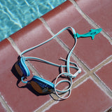 Sea foam green orca shaped Swim Loops goggle tag to label swim goggles attached to goggles next to swimming pool