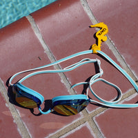 Yellow seahorse shaped Swim Loops goggle tag to label swim goggles with name written on it next to swimming pool