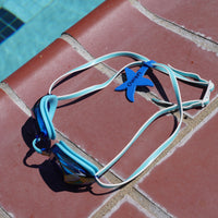 Blue starfish shaped Swim Loops goggle tag to label swim goggles with name written on it attached to swim goggles next to swimming pool