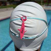 Dark pink shark shaped Swim Loops goggle tag to label swim goggles attached to swim goggles on swimmers head