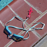 Dark pink shark shaped Swim Loops goggle tag to label swim goggles with name written on it attached to swim goggles next to swimming pool